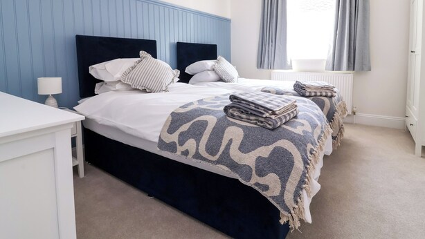 Cama bem arrumada com manta estampada, luminária de cabeceira e janela com cortinas.