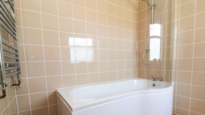 Casa de banho com banheira branca, chuveiro manual e porta-toalhas.