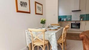 Uma sala de jantar com uma mesa posta para quatro pessoas, cadeiras de madeira, um vaso com flores e quadros nas paredes.