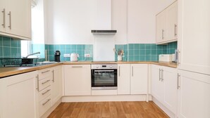 Uma cozinha moderna com armários brancos, forno de aço inoxidável e bancada de madeira.