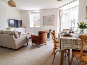 Ein Wohnzimmer mit einer Couch, einem braunen Ledersessel, einem Esstisch mit Tellern, Gläsern und einer Blumenvase.