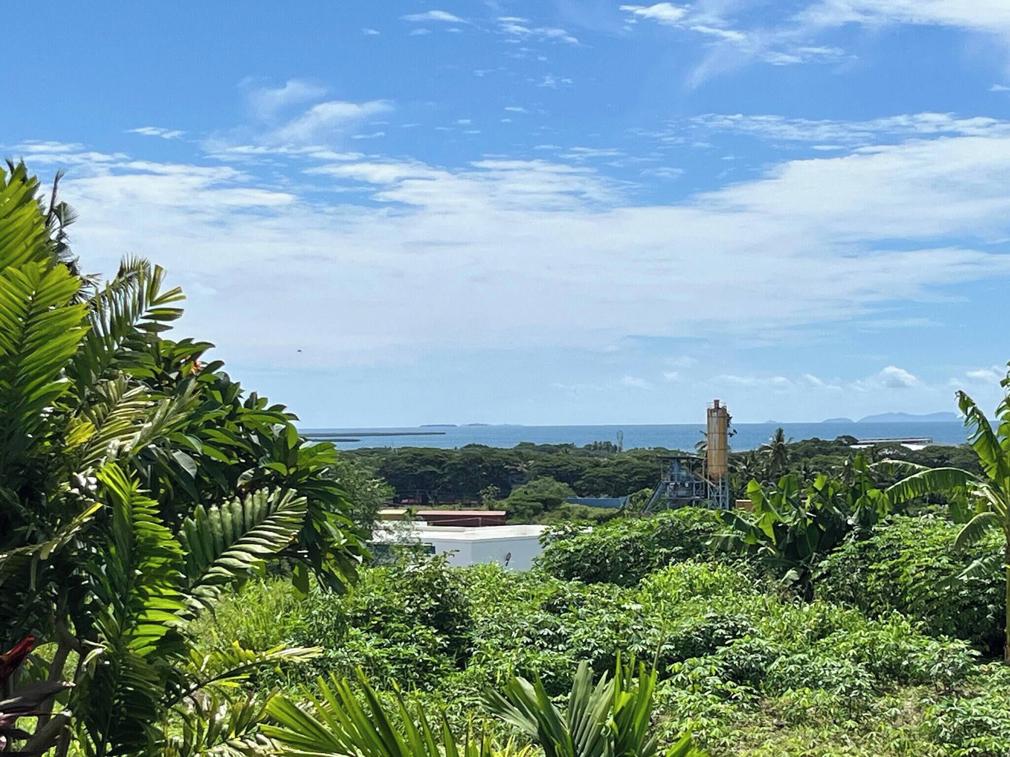 A lush green landscape with a clear view of the ocean and distant islands.