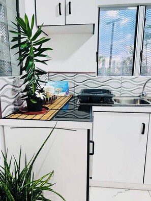 Una cocina moderna con armarios blancos, una estufa a gas, un lavamanos y una ventana con vistas a edificios.
