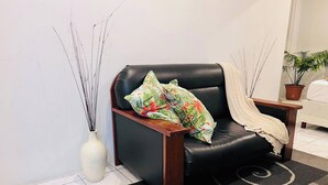 Un sillón de cuero negro con un cojín floral, un jarrón blanco con tallos largos y una planta en maceta en un rincón.