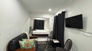 Habitación de hotel compacta con cama, escritorio, silla, sofá y televisor montado en la pared.