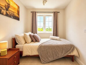 Ein Schlafzimmer mit einem Bett, einem Nachttisch, einer Lampe und einem Fenster mit Vorhängen.