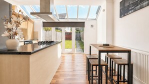 A modern kitchen with a central island, wooden flooring, and a view of the backyard through a glass door. - Modern 3BDR Family House in North Stifford (North Stifford)