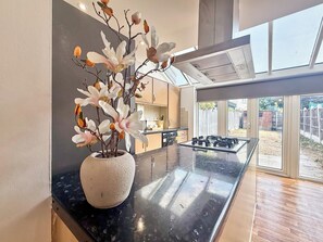 A modern kitchen with a central island, a potted plant, and a view of the backyard through large sliding doors. - Modern 3BDR Family House in North Stifford (North Stifford)