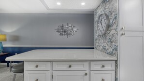 Une pièce avec un comptoir blanc, des tiroirs, une horloge au mur et un papier peint à motifs.