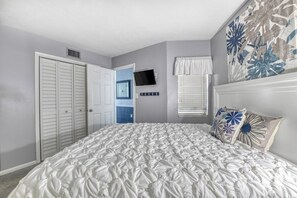 Ein Schlafzimmer mit einem großen Bett, einem Kleiderschrank, einem Fernseher und einem Fenster mit Jalousien.