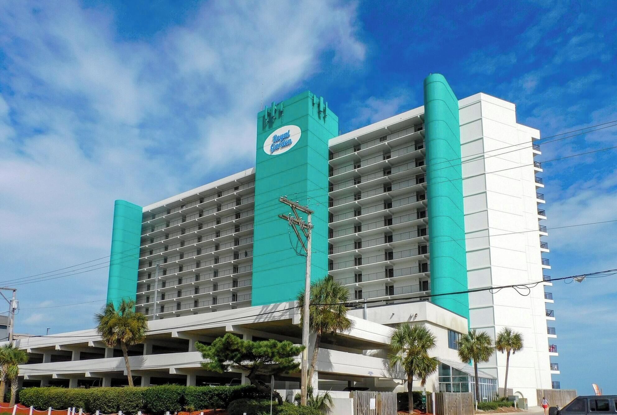 A multi-story hotel with a prominent green and white color scheme, featuring a large sign with a logo and the name 'Hotel' visible on the facade.