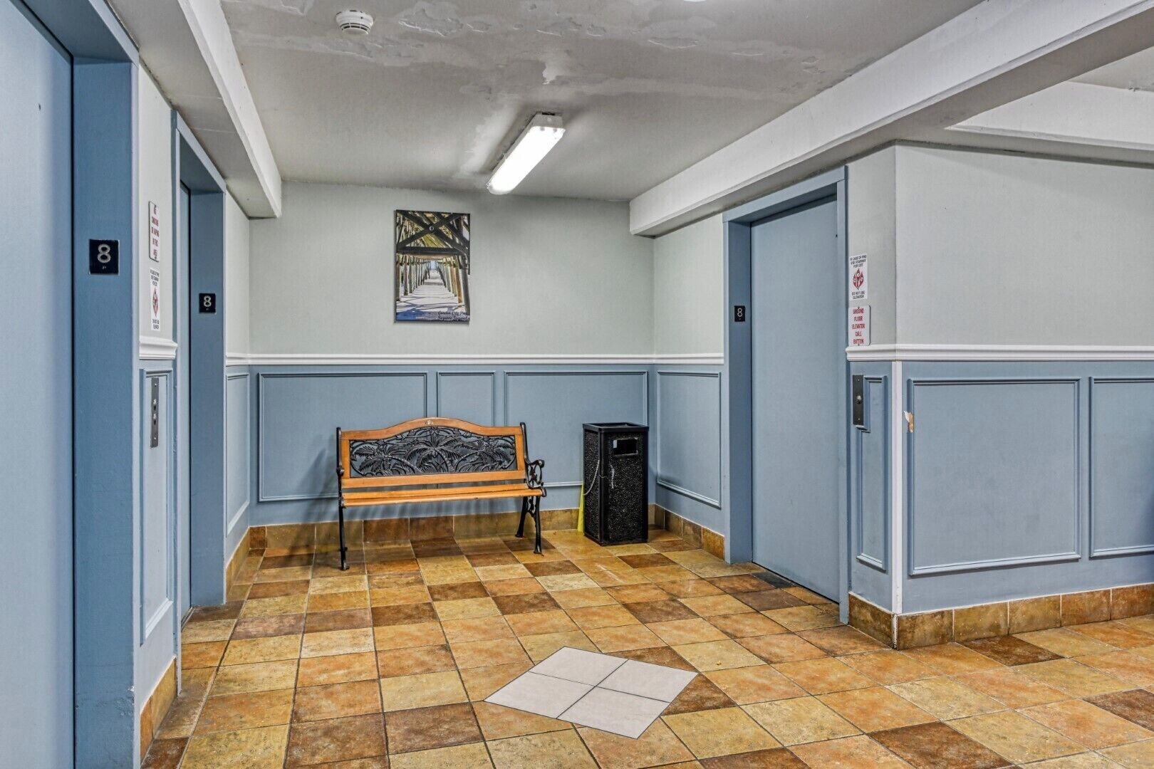 A hallway with blue walls, a bench, a trash bin, and doors marked with the number 8.