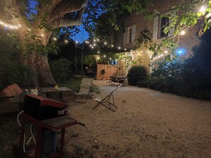 An outdoor patio area with string lights, a table, chairs, and a grill. - Renovated Provençal farmhouse in a quiet setting – 2 hectares of wooded land (Sarrians)