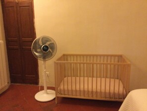 A room with a wooden crib, a white fan, and a radiator.