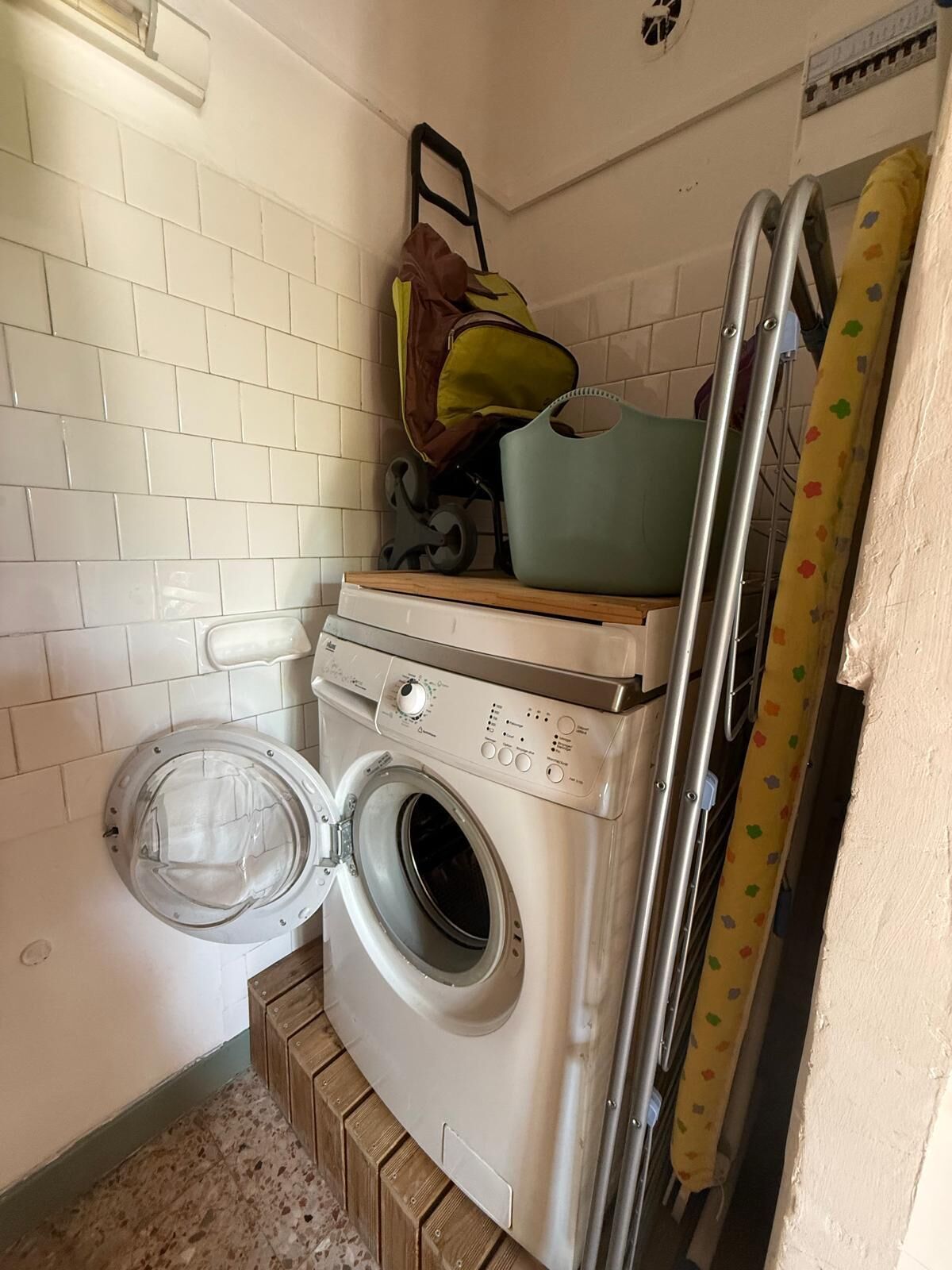 Een kleine wasruimte met een voorlader wasmachine, een droogrek en een kinderwagen.