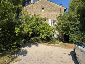 A stone building with a gravel driveway and a parked car. - Renovated Provençal farmhouse in a quiet location—2 hectares of wooded land (Sarrians)