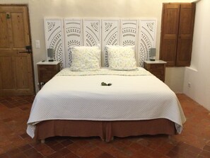 A bed with a white quilt, two pillows, a nightstand with a lamp, and a wooden headboard. - Renovated Provençal farmhouse in a quiet setting – 2 hectares of wooded land (Sarrians)