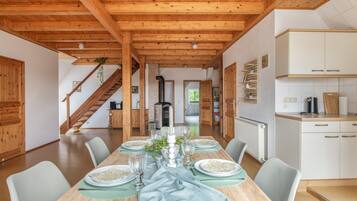 A dining area with a long wooden table set for a meal, flanked by chairs, with a staircase leading to another room.