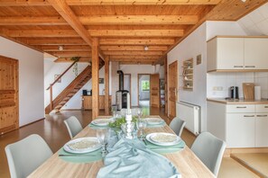 Un espace repas avec une longue table en bois dressée pour le repas, entourée de chaises, et un escalier menant à une autre pièce.