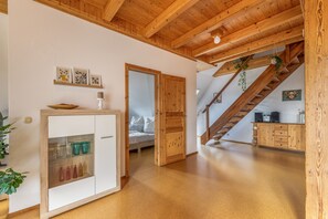 A spacious room with a wooden ceiling, a bed with white bedding, a wooden staircase, and a cabinet with glassware.