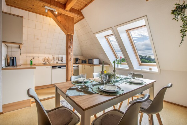 A modern kitchen with a dining area, featuring a wooden ceiling, skylights, and a view of the outdoors.