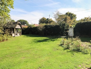 A grassy yard with a wooden structure, possibly a gazebo, surrounded by trees and a fence.