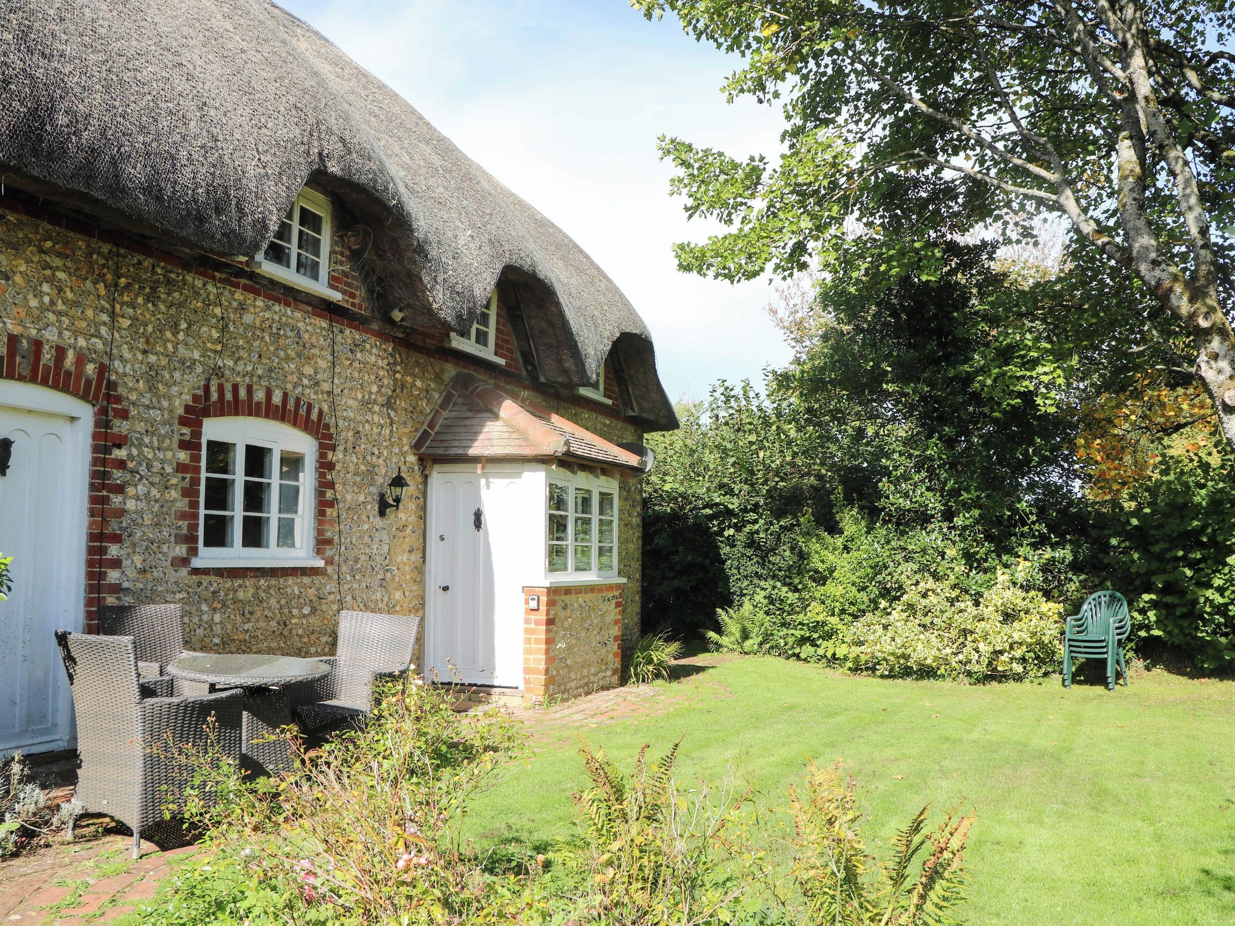 A traditional stone house with a thatched roof, a brick chimney, and a small garden with a lawn and a chair.