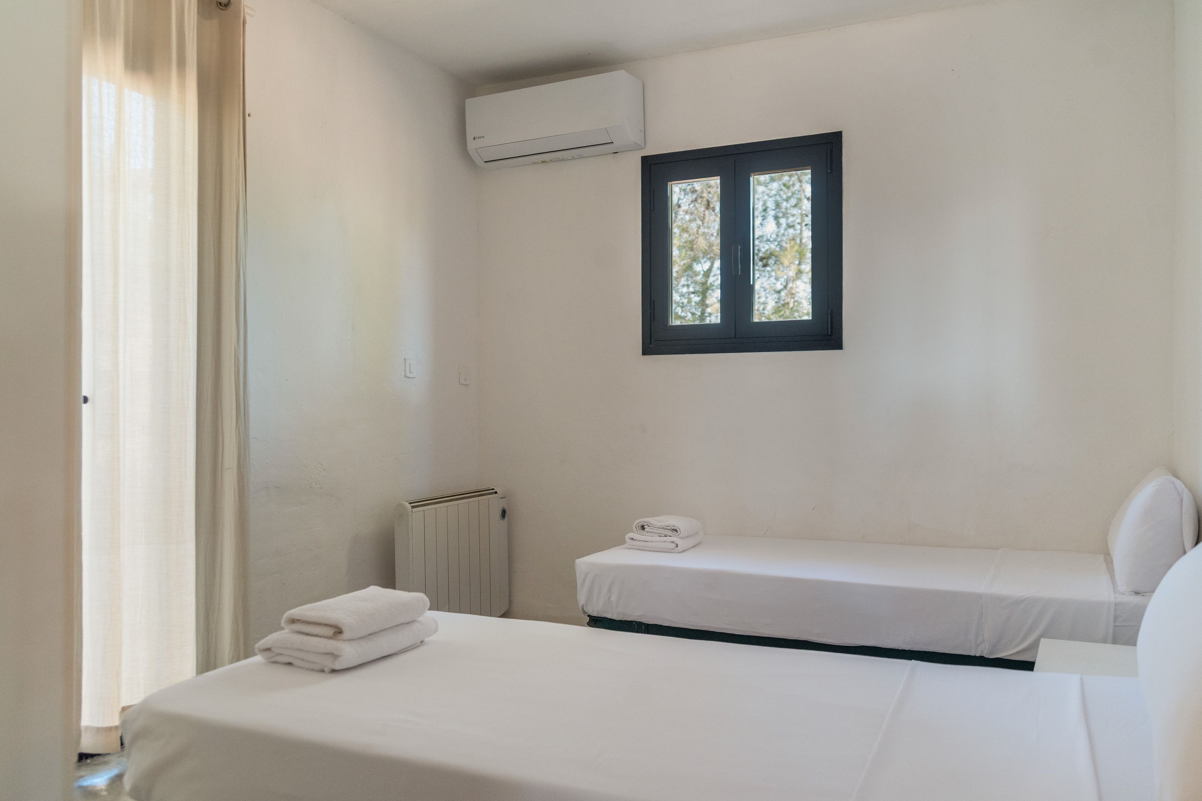 Une chambre simple avec deux lits, une fenêtre, un climatiseur et un radiateur.