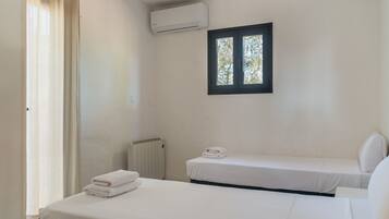 Une chambre simple avec deux lits, une fenêtre, un climatiseur et un radiateur.