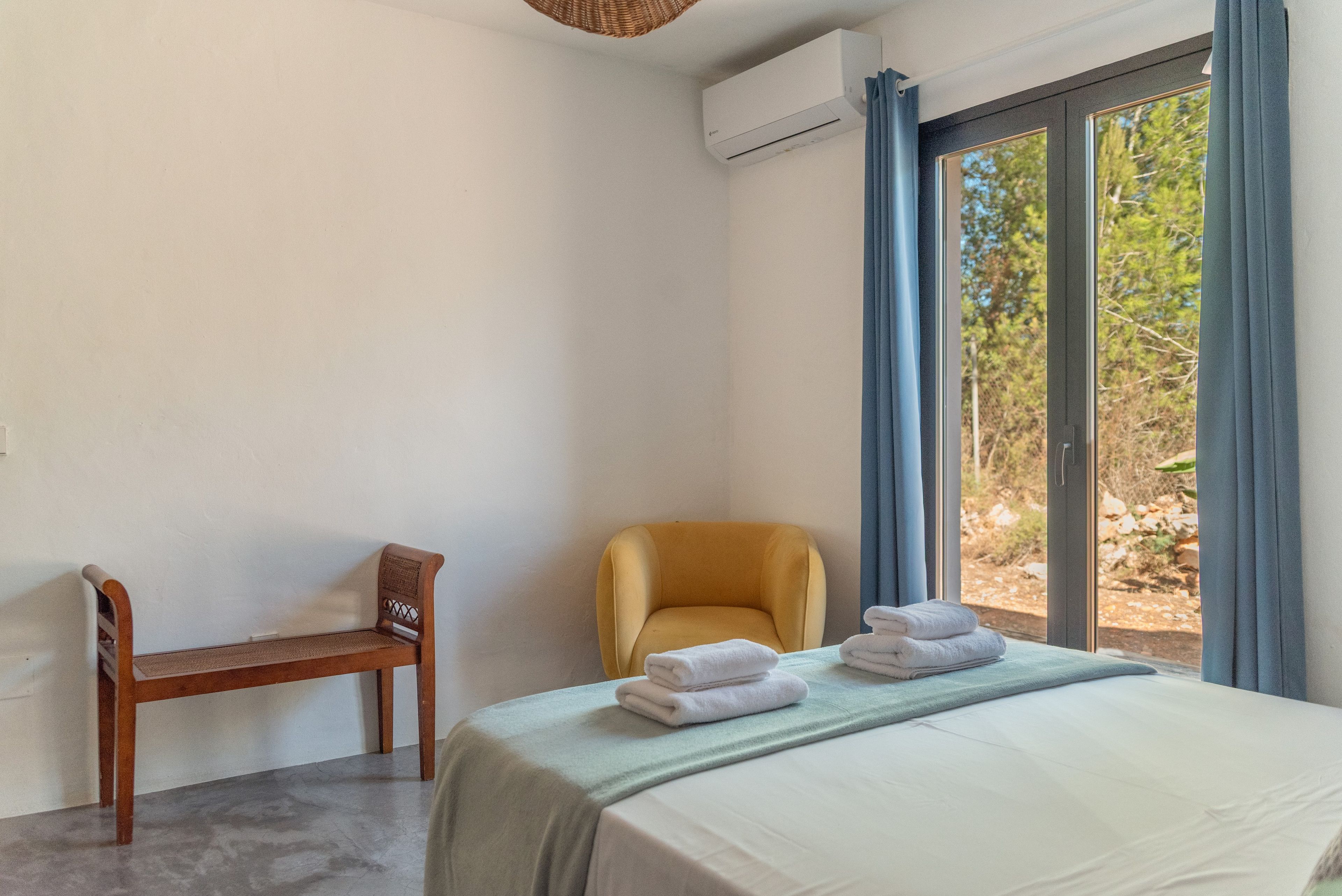 A bedroom with a bed, a chair, and a view of the outdoors through a window.