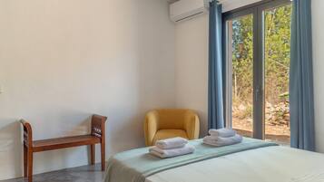 A bedroom with a bed, a chair, and a view of the outdoors through a window.