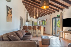 Un interior moderno con un sofá, taburetes de bar, un televisor y una zona de cocina.