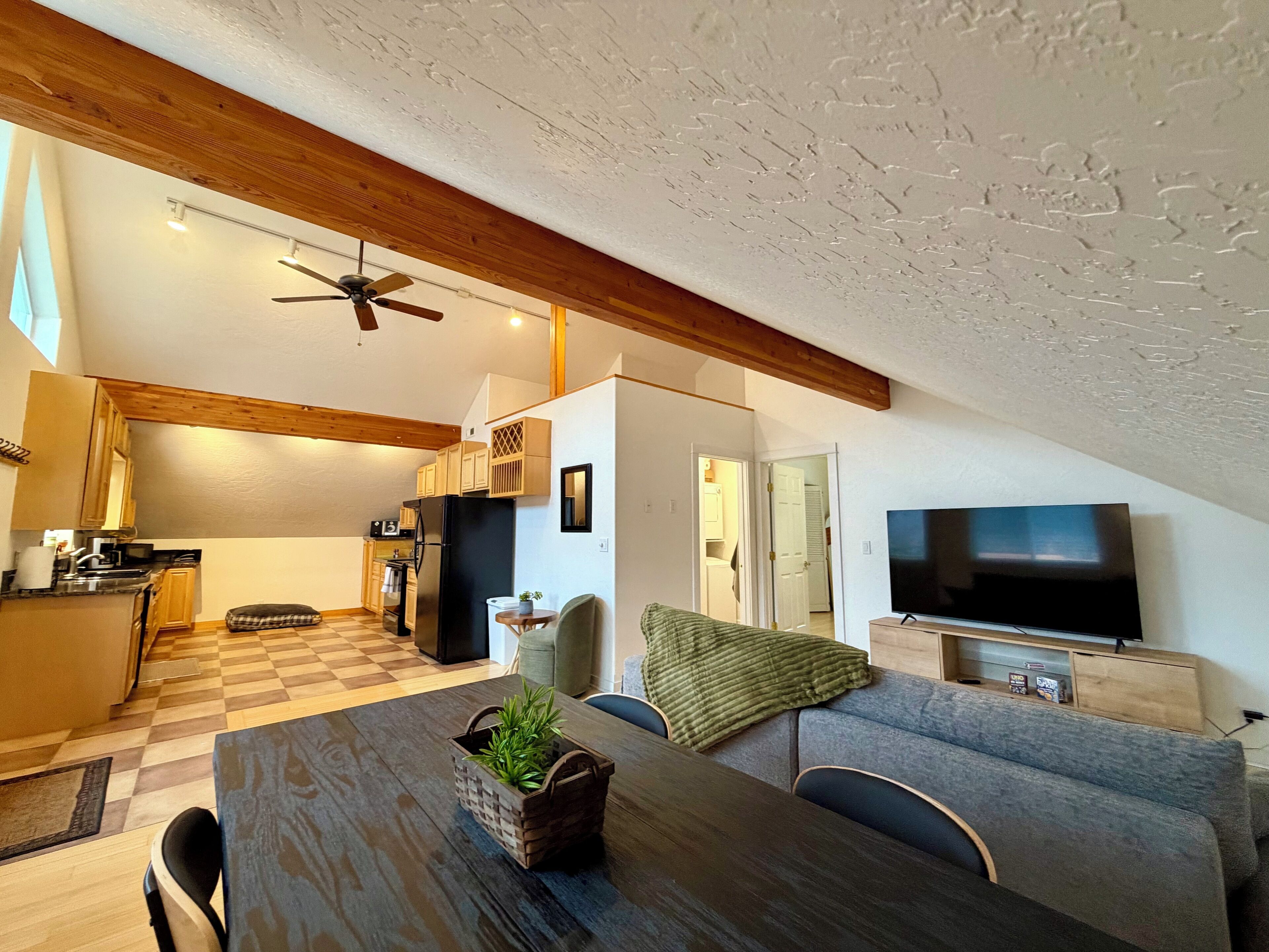 Un espacio habitable compacto con cocina, comedor y zona de estar, que presenta vigas de madera, ventilador de techo y televisor de pantalla plana.