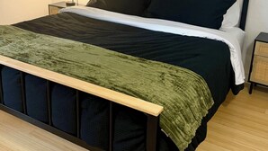 Un lit avec un cadre en bois, une couverture verte et du linge de lit noir.