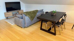 Un espace de vie moderne comprenant un canapé, un téléviseur, un plancher en bois et une table à manger avec des chaises.
