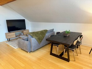 Un espace de vie moderne comprenant un canapé, un téléviseur, un plancher en bois et une table à manger avec des chaises.