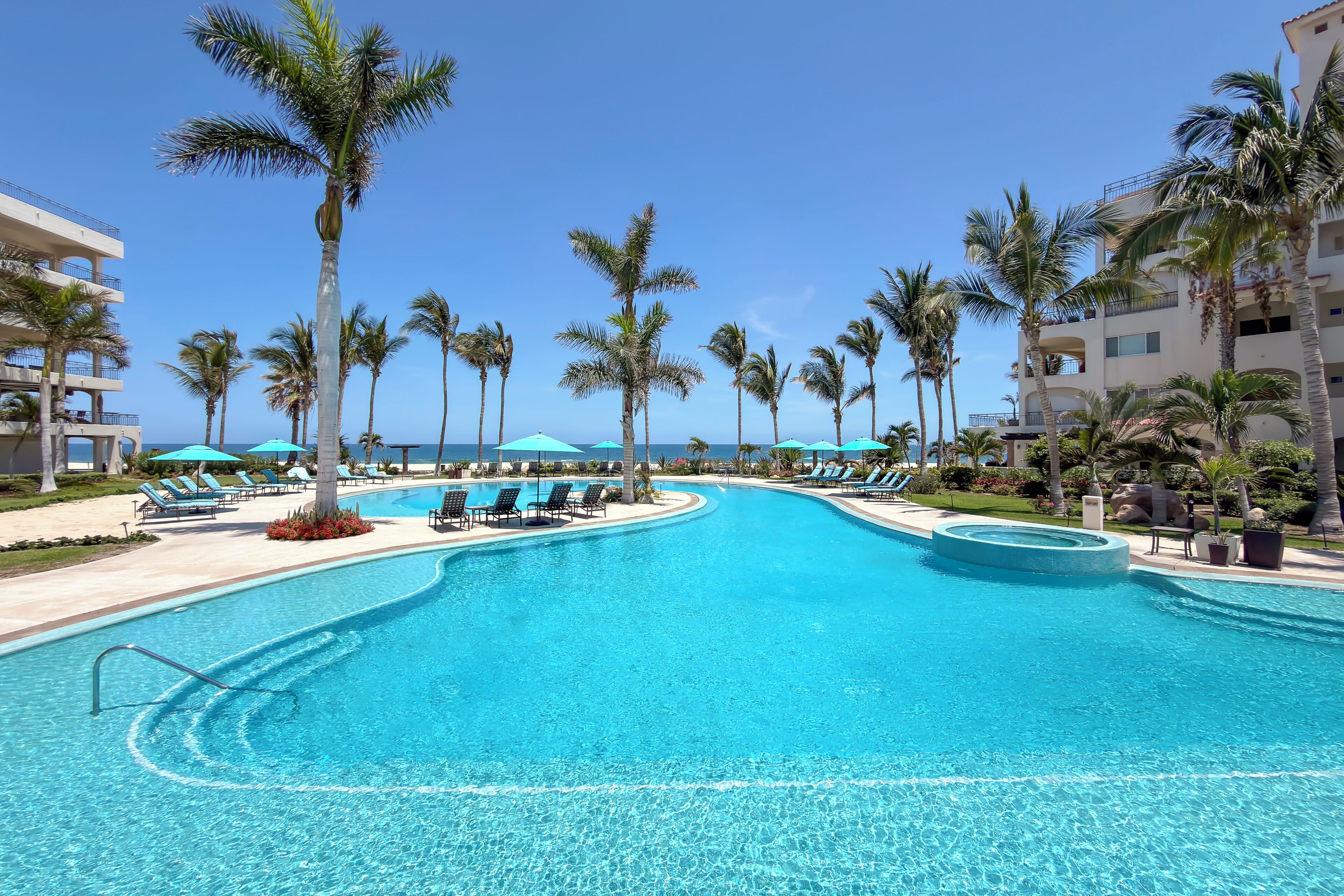 A swimming pool with lounge chairs and palm trees, surrounded by buildings.
