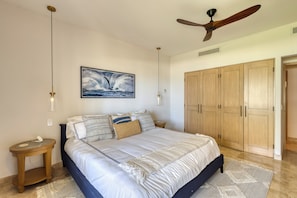 Ein Schlafzimmer mit einem großen Bett, einem Deckenventilator, einem an der Wand befestigten Bild und einem Holzschrank.