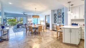 A spacious living area with a dining table, chairs, and a kitchen with white cabinets and a marble countertop. - Azure at Tortuga Bay | Luxury Beachfront Condo (San Jose Del Cabo)