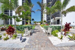 A pathway leading to a building with a modern design, surrounded by palm trees and plants. - 🏖️Gulf Views | Steps to Beach | Beachfront Complex | Island Winds 1003 🏖️ (Fort Myers Beach)