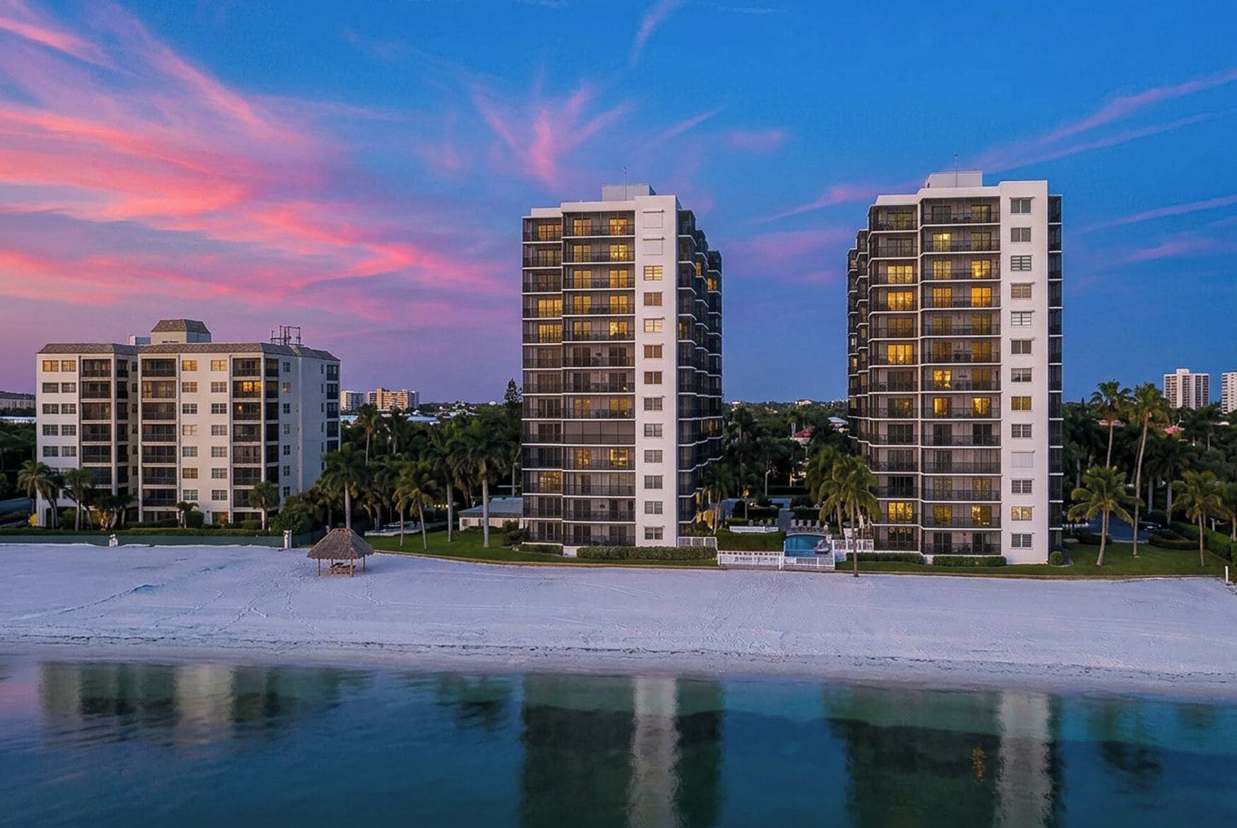 Un hotel frente a la playa con varias torres, una piscina y palmeras.