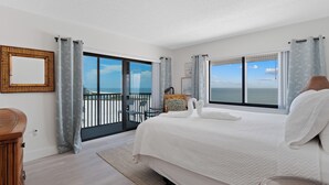 Quarto de hotel com uma cama grande, vista para o mar e varanda com guarda-corpo.