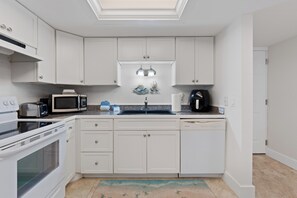 Eine moderne Küche mit weißen Schränken, einem Backofen, einer Mikrowelle, einer Kaffeemaschine und einem Spülbecken.