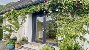 A house with a glass door, a small outdoor seating area, and various potted plants. - Cuil Steading -  Spectacular Loch Views & Garden (Cairndow)