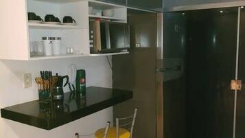 Una cocina compacta con encimera negra, dos sillas amarillas, microondas y refrigerador de acero inoxidable.