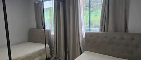A room with two beds, a sofa, and a window with curtains.