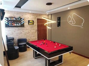Une table de billard avec des billes, un bar avec des bouteilles et un mur orné d’un logo.