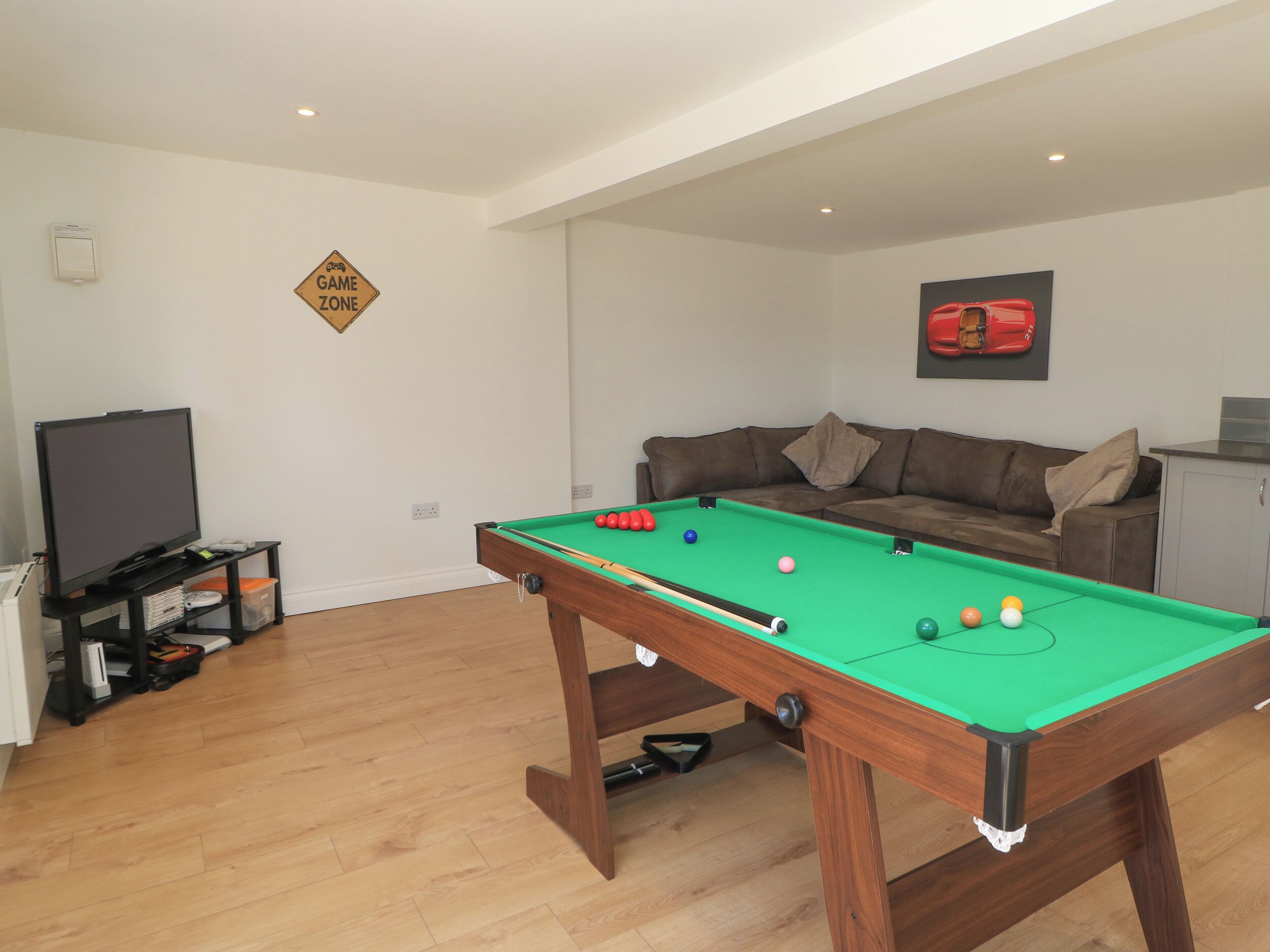 A room with a pool table, a sofa, a television, and a sign indicating a game zone.