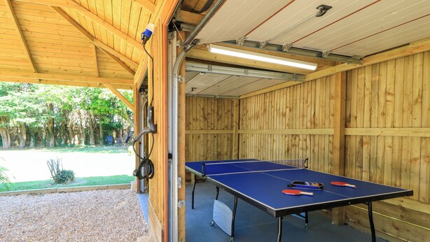 An indoor ping pong table with a table tennis paddle and ball, a blue table tennis paddle, and a red paddle. - Cern-wyn (Chippenham)