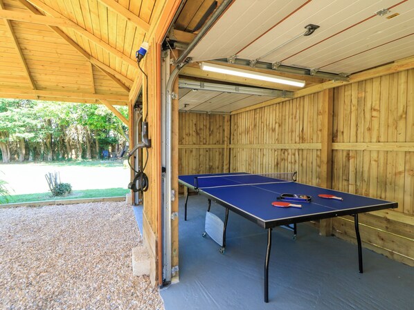 An indoor ping pong table with a table tennis paddle and ball, a blue table tennis paddle, and a red paddle.